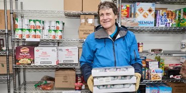 A GCFP volunteer restocks shelves wearing a blue jacket and a smile.