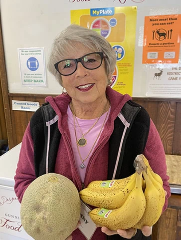 A volunteer lady holding a cantaloupe and bananas at the Gunnison Country Food Pantry.