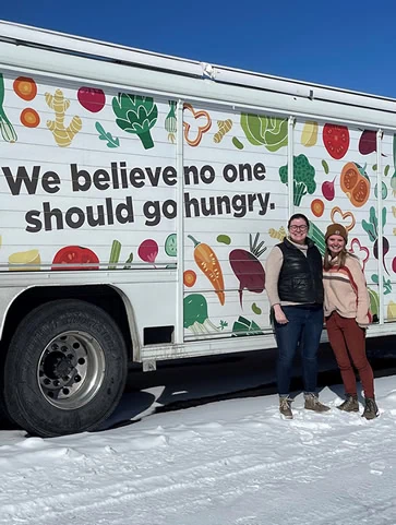 GCFP Staff are standing in the snow beside a delivery truck that says, "We believe no one should go hungry."