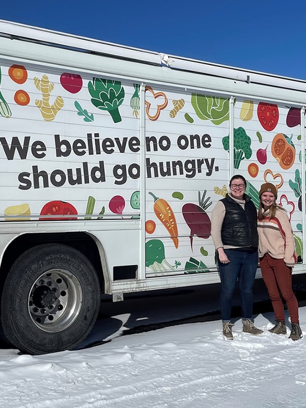 Two of Gunnison Country Food Pantry's staff standing by a truck that says, "We believe no one should go hungry".