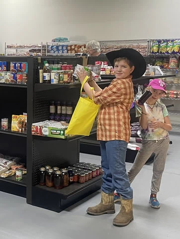 Boy in cowboy hat and cowboy boots and his little sister picking groceries out from the Pantry shelves.