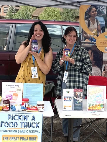 Volunteers hold up peanut butter and jelly jars at a mobile pantry event.
