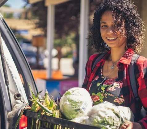 Young lady holding a basket of fresh vegetables by a mobile delivery vehicle.