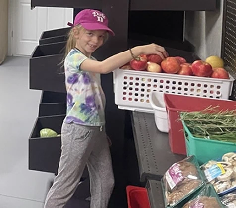 A young girl volunteers and picks out apples from a bin.