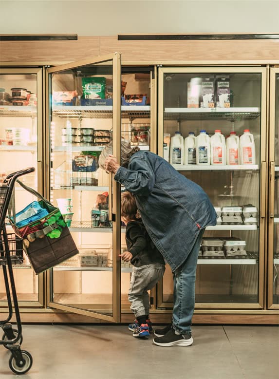 A grandmother and grandchild shop from a refrigerated cooler.