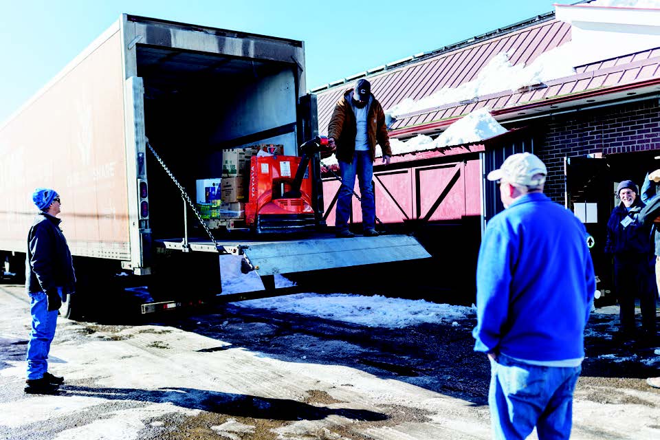 A group of volunteers unload a semi truck food delivery in the snow with clear blue skies.