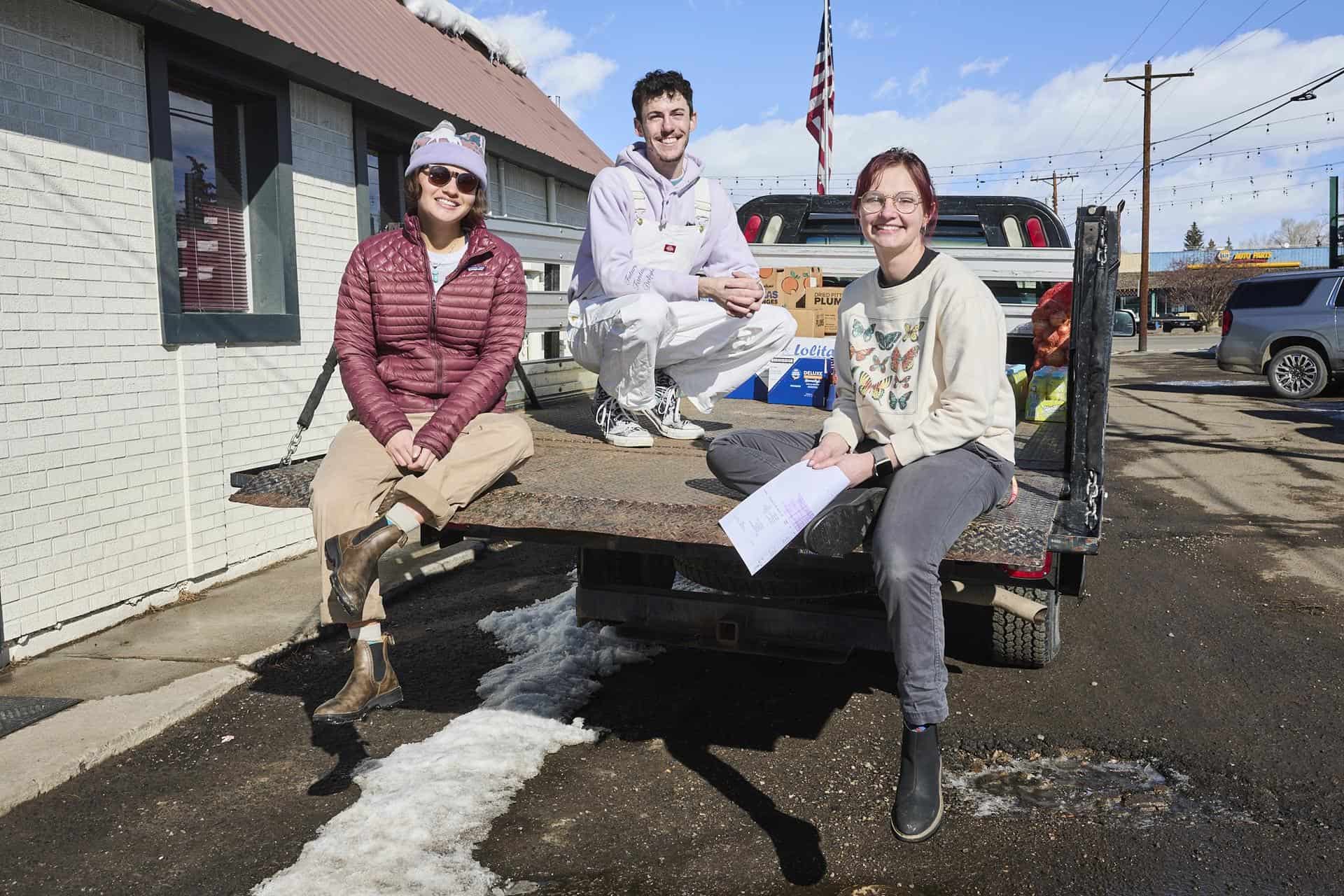 Three students smile from the back of a pickup truck parked in a snowy Food Pantry parking lot.