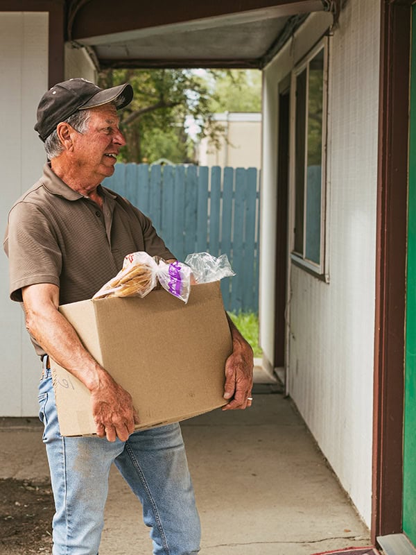 Next Step Network A male volunteers brings a box of food to a person's doorstep.