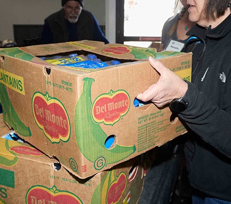A volunteer moves a large box of bananas onto a stack of boxes.