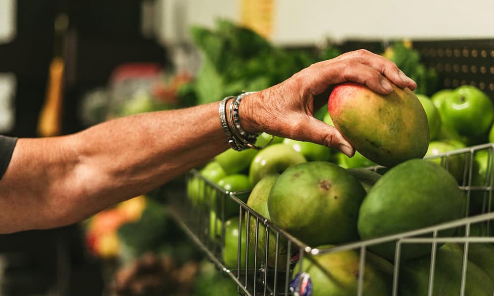 081425 No One Goes Hungry 2 1000x600 A woman's hand is selecting a mango from a basket.